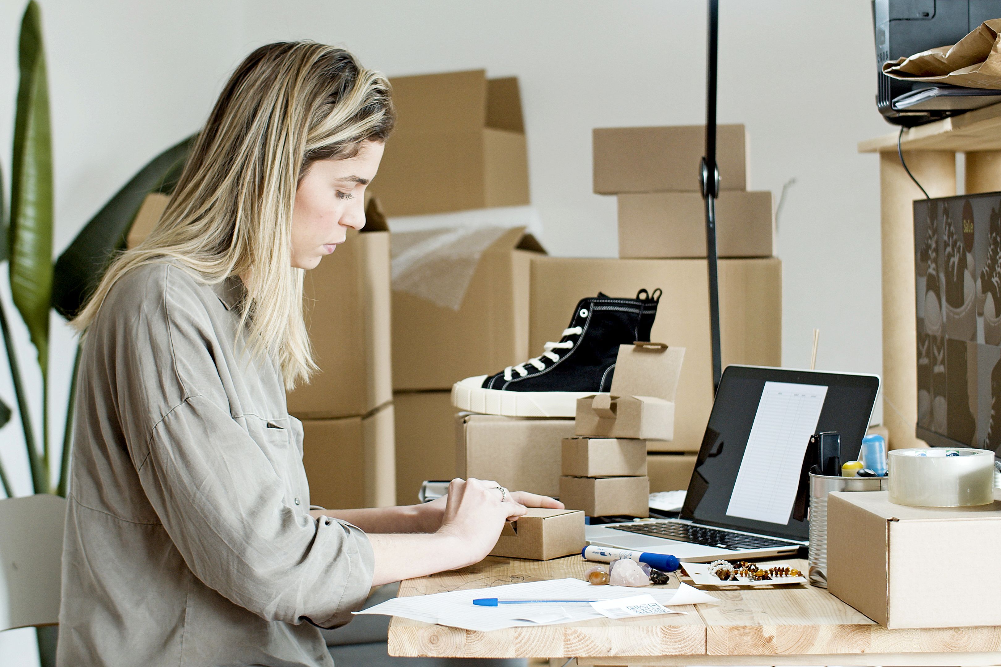 An online seller preparing a cardboard parcel beside her laptop